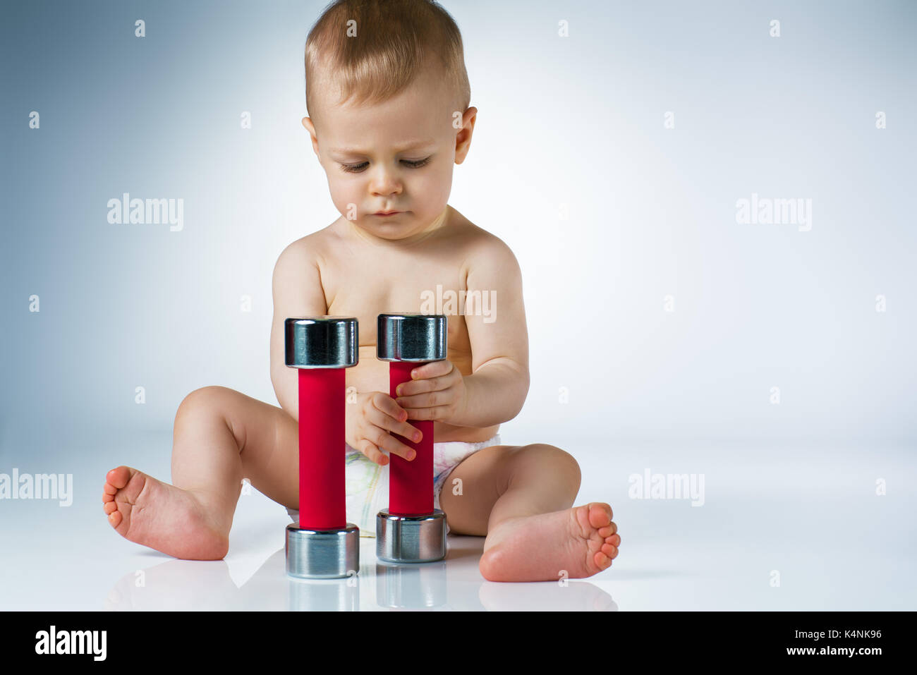 Eight month baby sitting and playing with dumbbells on white background Stock Photo