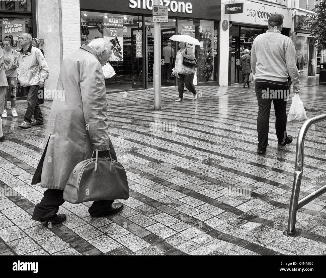 Old man carrying wearing overcoat walking through Leeds city centre. UK Stock Photo