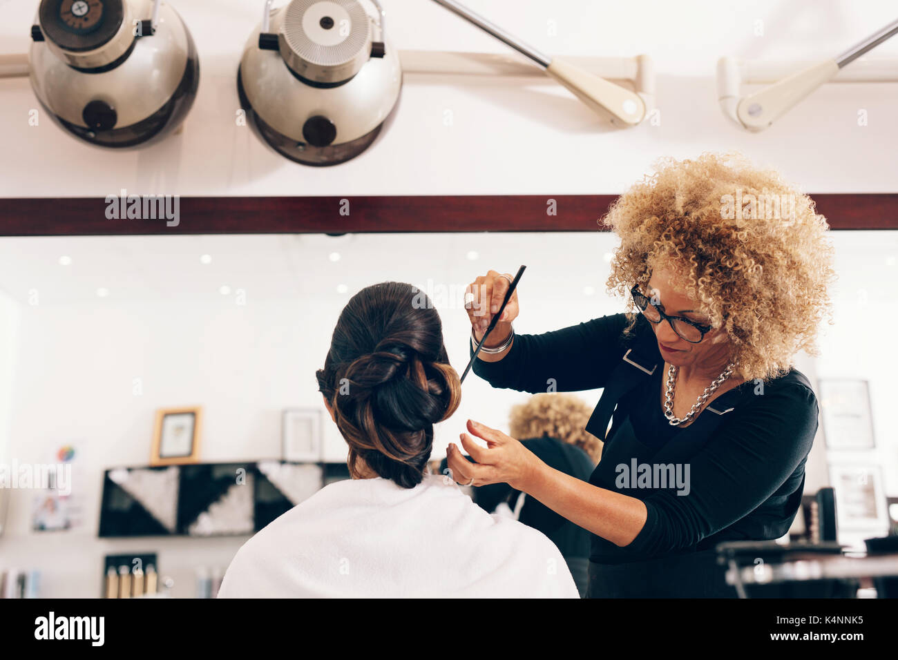 Professional hairdresser styling the hair of a customer at salon. Female hair stylist setting hair in fashionable design. Stock Photo