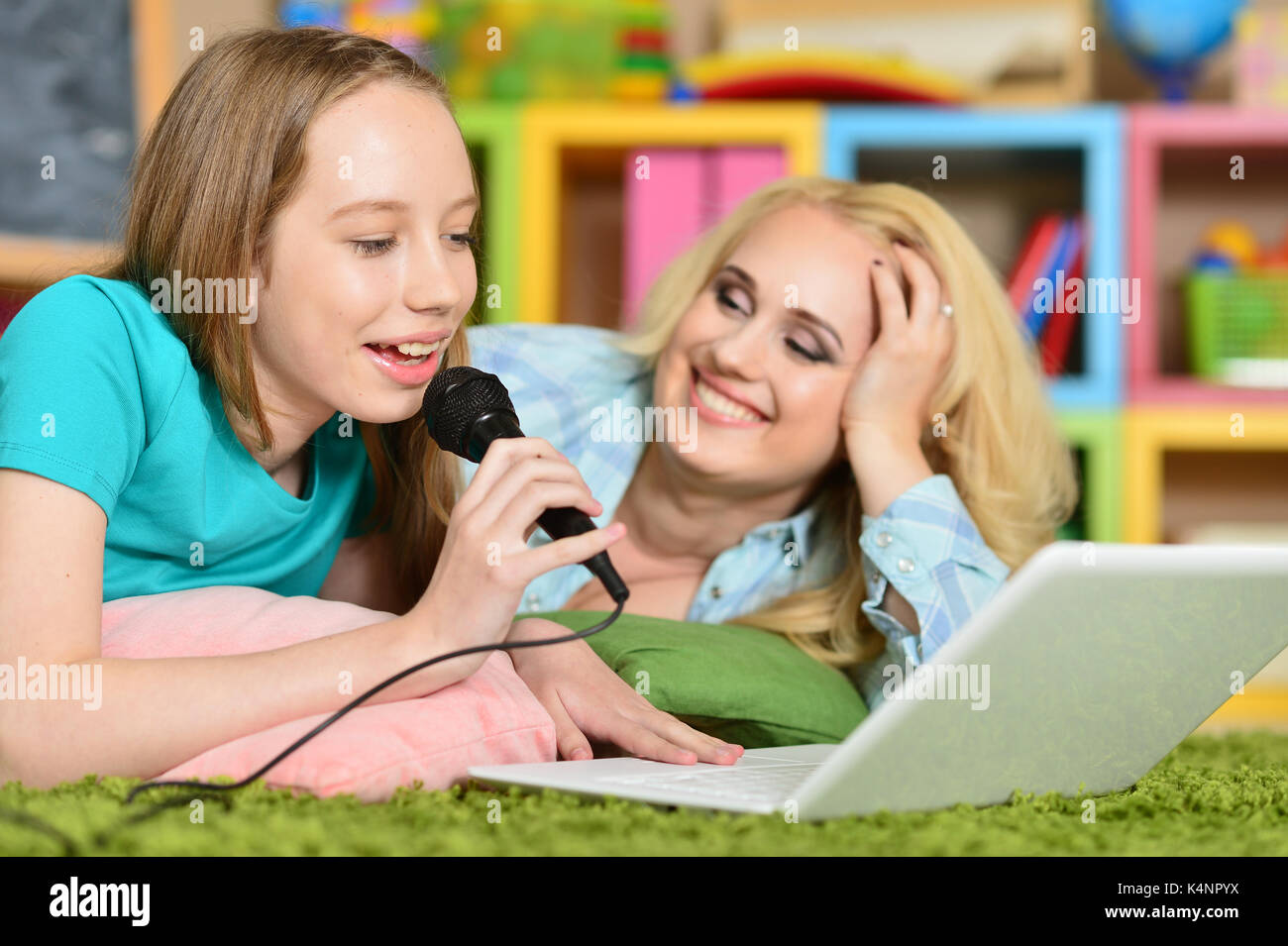 Mother And Daughter Lying On Floor And Singing Karaoke Together Stock