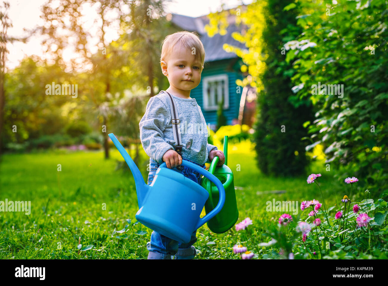 One year cute child in summer garden with two watering cans at sunset
