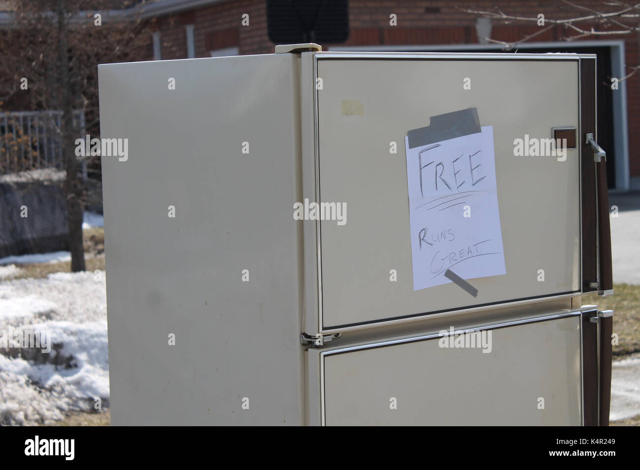 An old refrigerator on the curb of a residential property in Barrie Ontario with a sign that says 'Free Runs Great' Stock Photo
