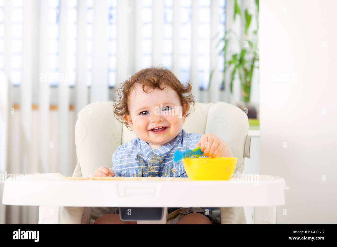 Cute baby boy eating by himself on high chair Stock Photo