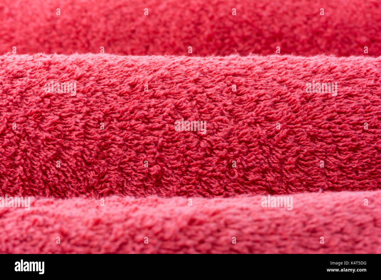 Abstract textures suitable for a background, depicting three rolled up, red terry towelling towels, in close up and cropped view. Focus is on the midd Stock Photo