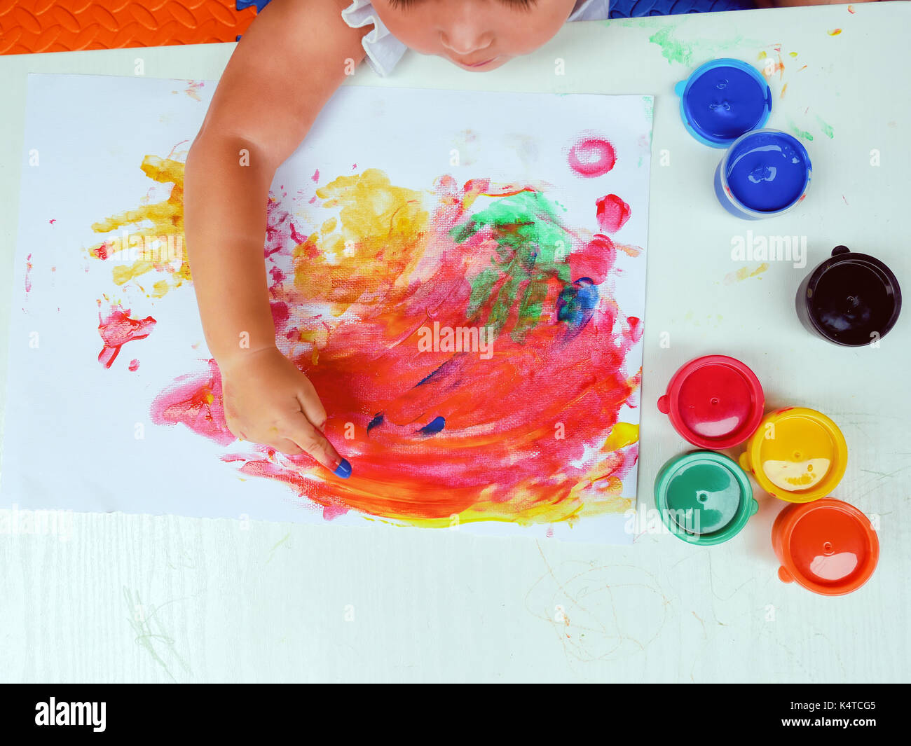 Little girl painting by finger hand paint color ,unlimited boundless imagination through Colorful coloring posters blended on a holiday desk that does not go to school.children development concept. Stock Photo