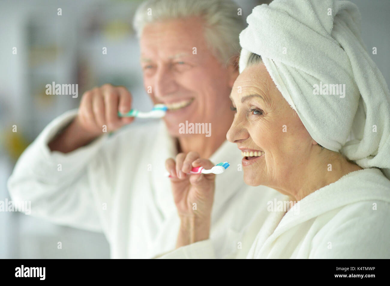 happy senior couple in white bathrobes brushing teeth Stock Photo