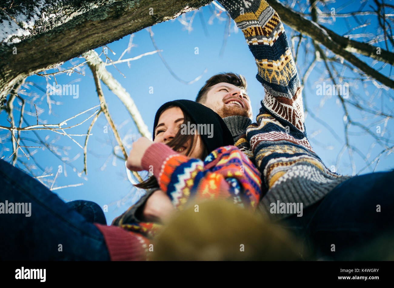 Joyful cute couple embraces. Young man in a sweater hugs a girl from sitting on tree branch in winter. The concept of a successful relationship and ha Stock Photo