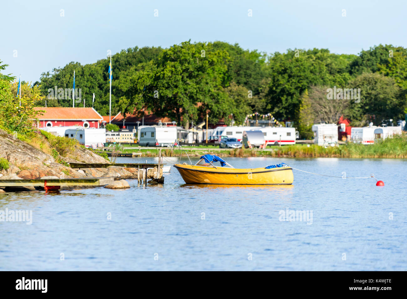 One open yellow motorboat moored to a pier with camping site in background. Location Karlskrona, Sweden. Stock Photo