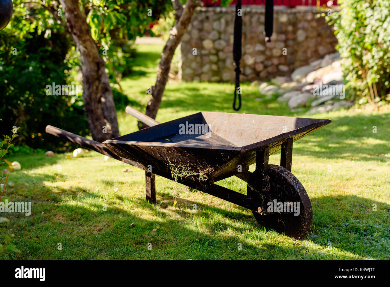 Old wooden wheelbarrow standing empty on lawn. Stock Photo