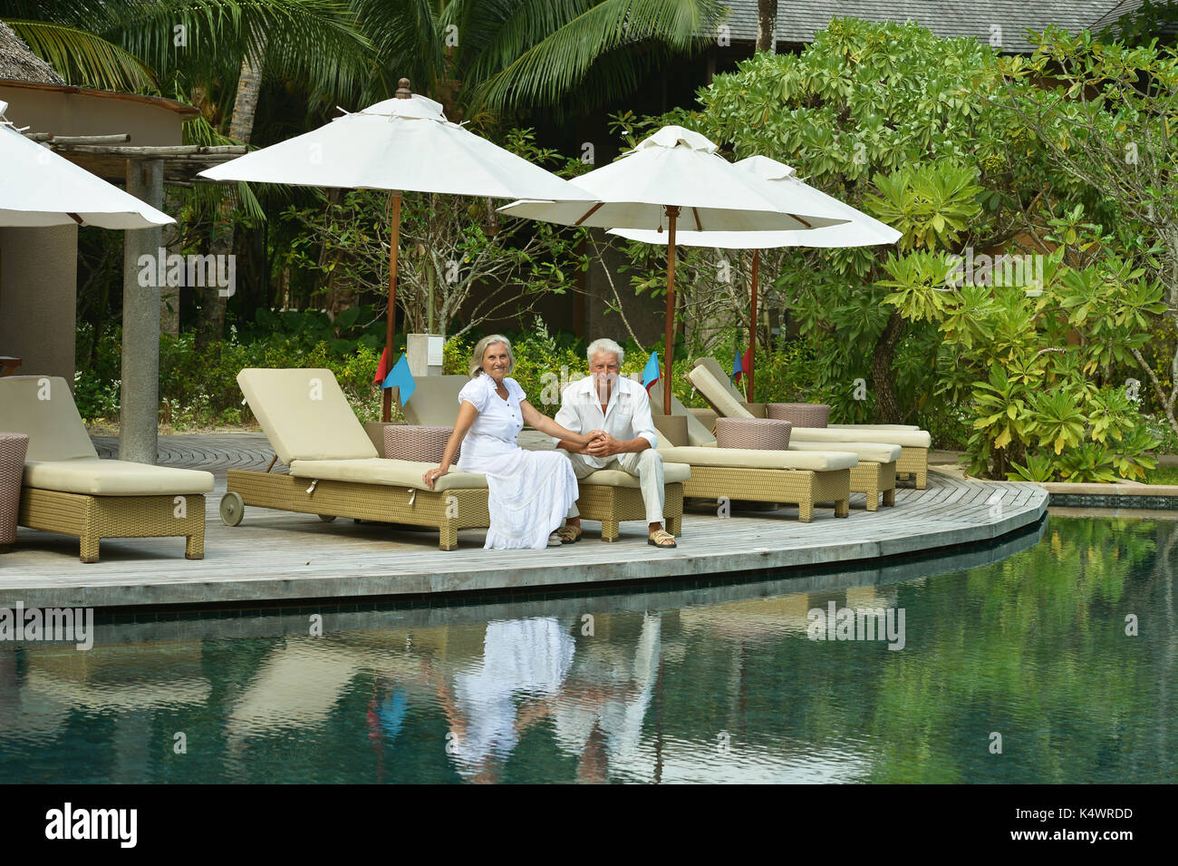 Smiling elderly couple sitting near swimming pool Stock Photo - Alamy