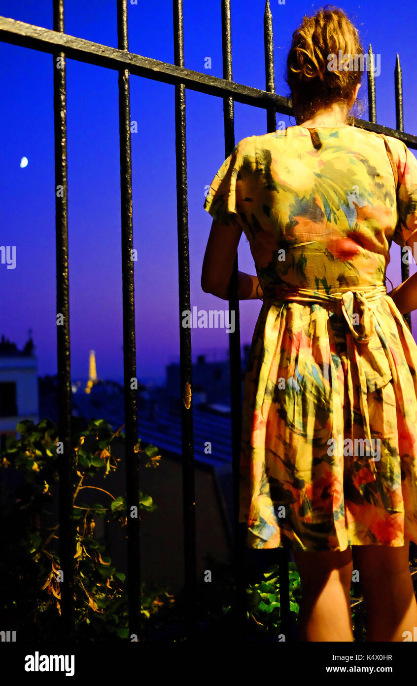 A lone young woman looks at the Eiffel Tower in the distance from the hill of Montmartre, close to Sacre Couer Stock Photo