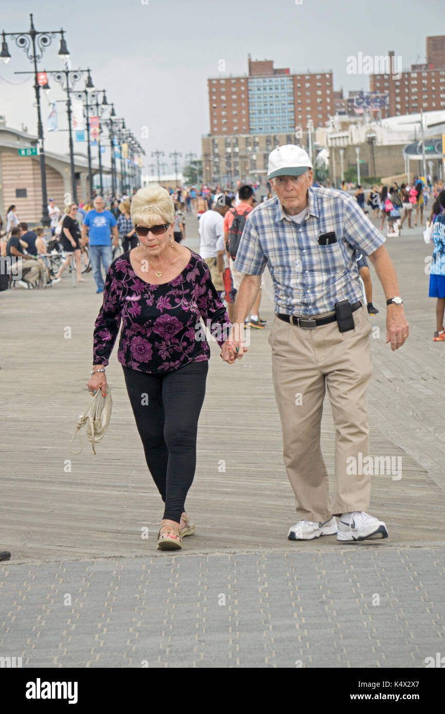 An elderly couple, perhaps in their eighties, holding hands while walking on the boardwalk in COney Island, Brooklyn, New York, on a late summer day. Stock Photo