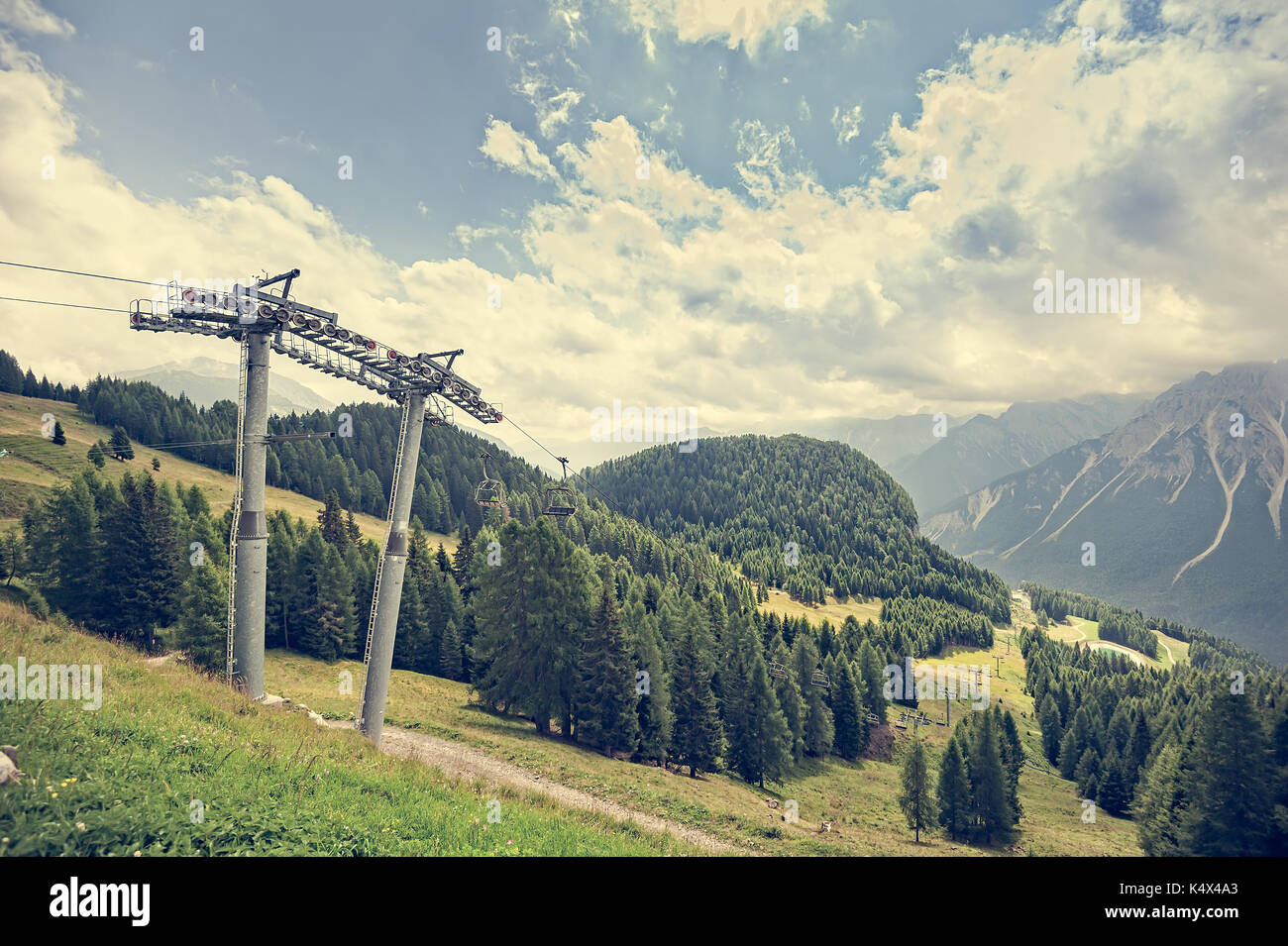 Mountain panorama with forest, Dolomites, valley and chairlift in summer. Sky with clouds. Photos with vintage effect filter. Stock Photo