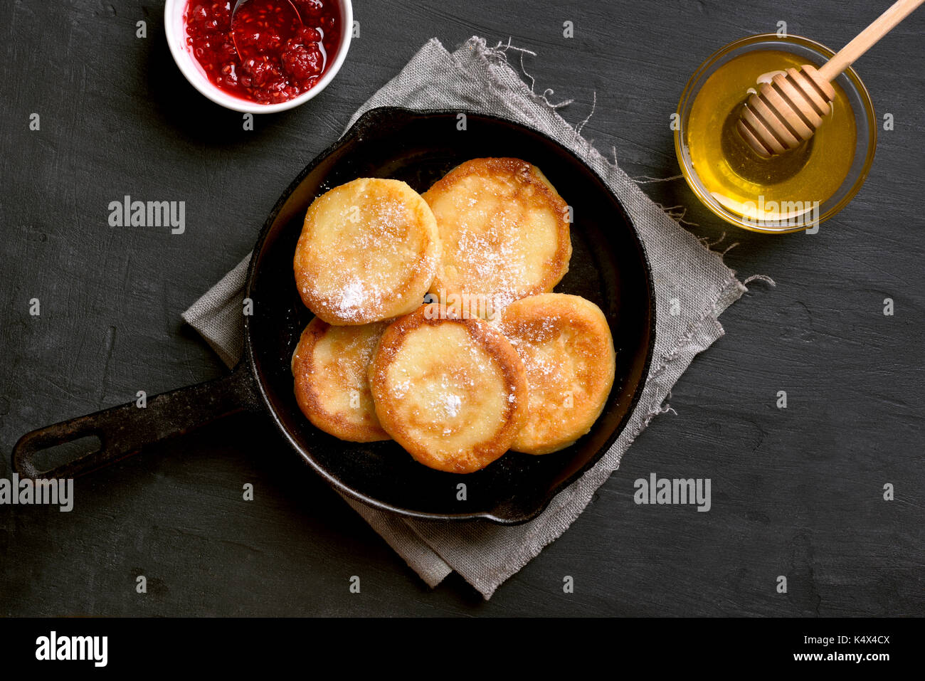 Fritters, curd cheese pancakes in cast iron pan on dark stone