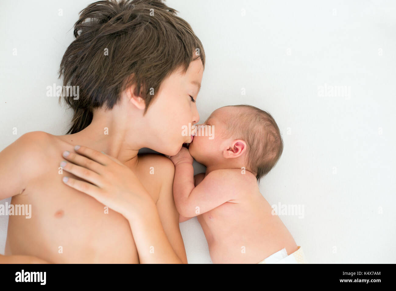 Beautiful boy, hugging with tenderness and care his newborn baby brother at home. Family love happiness concept Stock Photo
