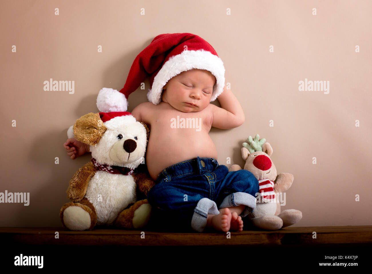 Newborn baby boy wearing a christmas hat and jeans, sleeping on a shelf next  to Teddy Bears. Shot in the studio on a creamy background, shot from abov  Stock Photo - Alamy
