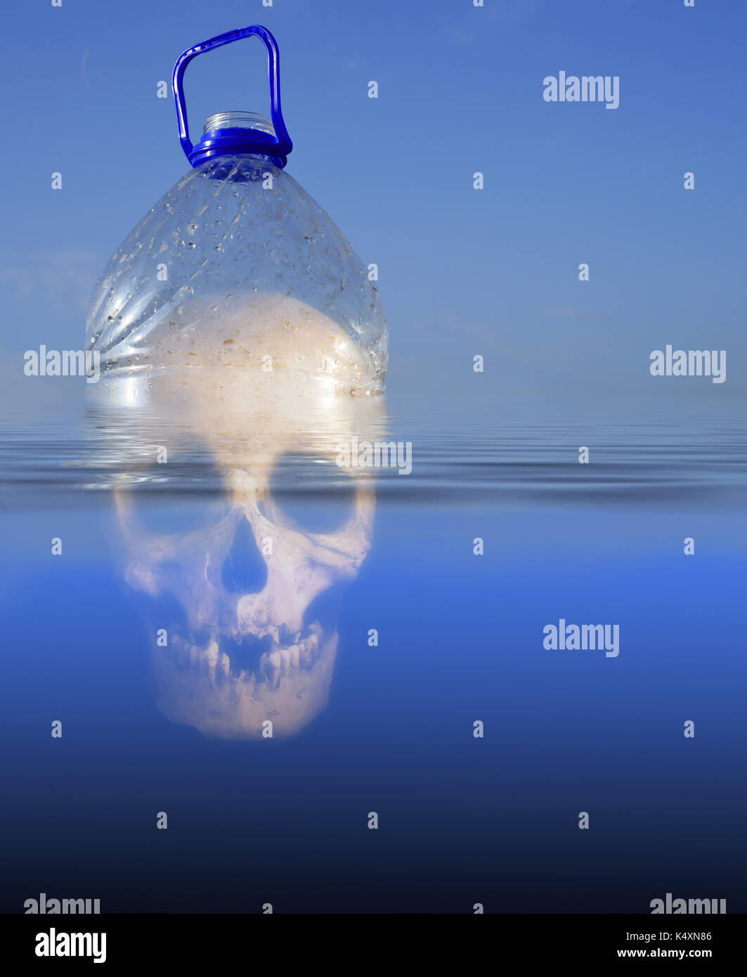 Pollution themed design of a plastic PET drinking container floating in sea water with a human skull submerged beneath the environment Stock Photo
