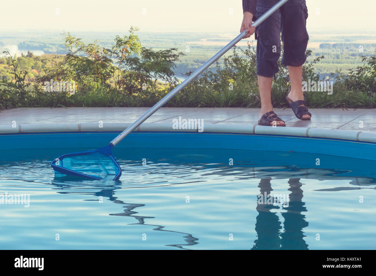 Man cleaning swimming pool of fall leaves with cleaning net in the