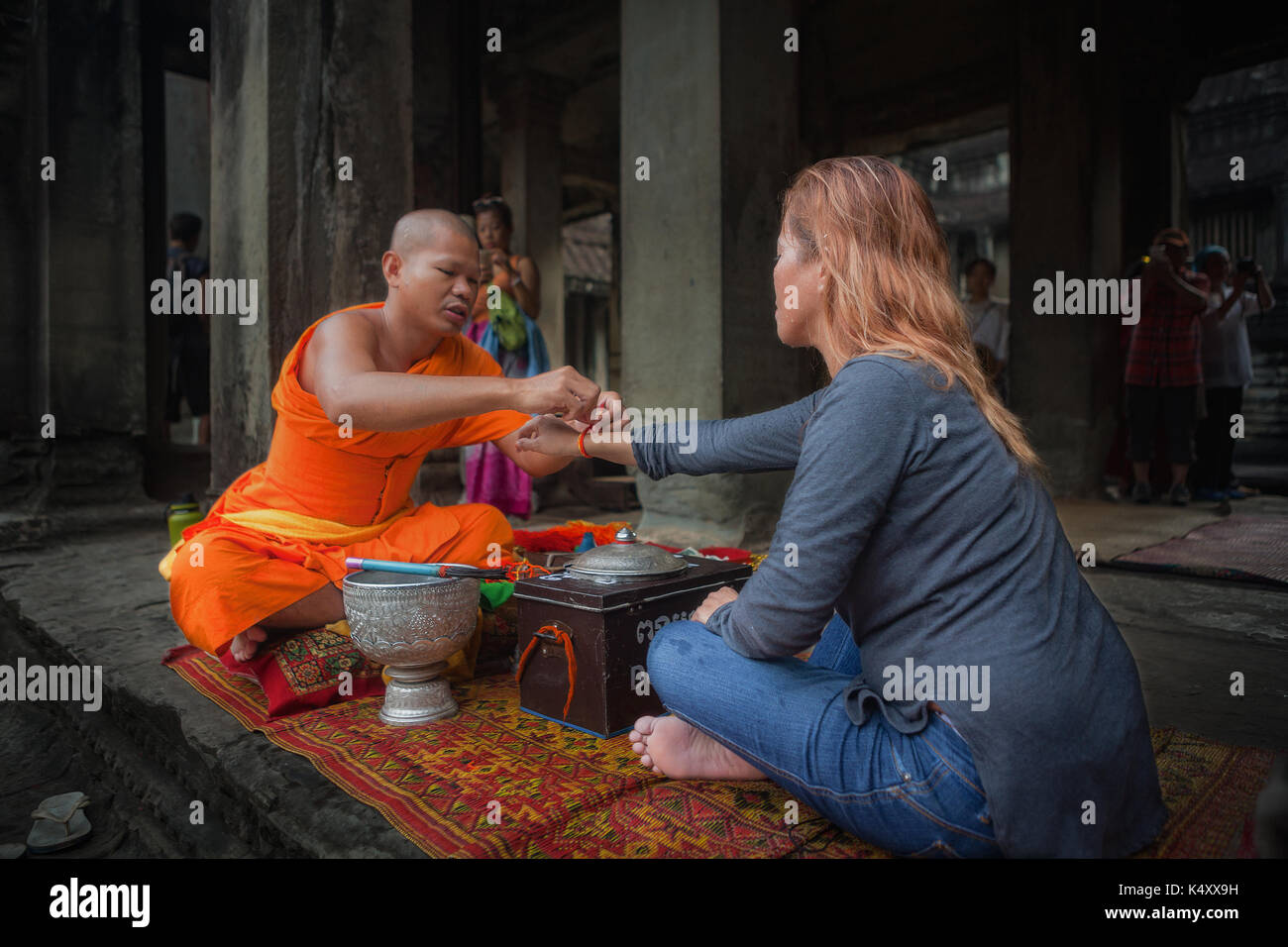 A tourist at Angkor Wat temple complex receives a blessing from a Buddhist monk. The temple complex is located in Siem Reap, Kingdom of Cambodia. Stock Photo
