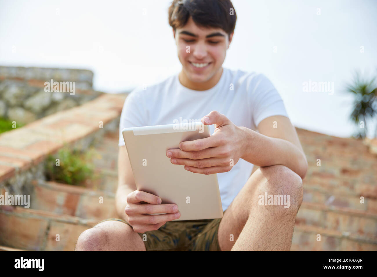 Portrait of young happy man sitting on stairs outside using tablet ...