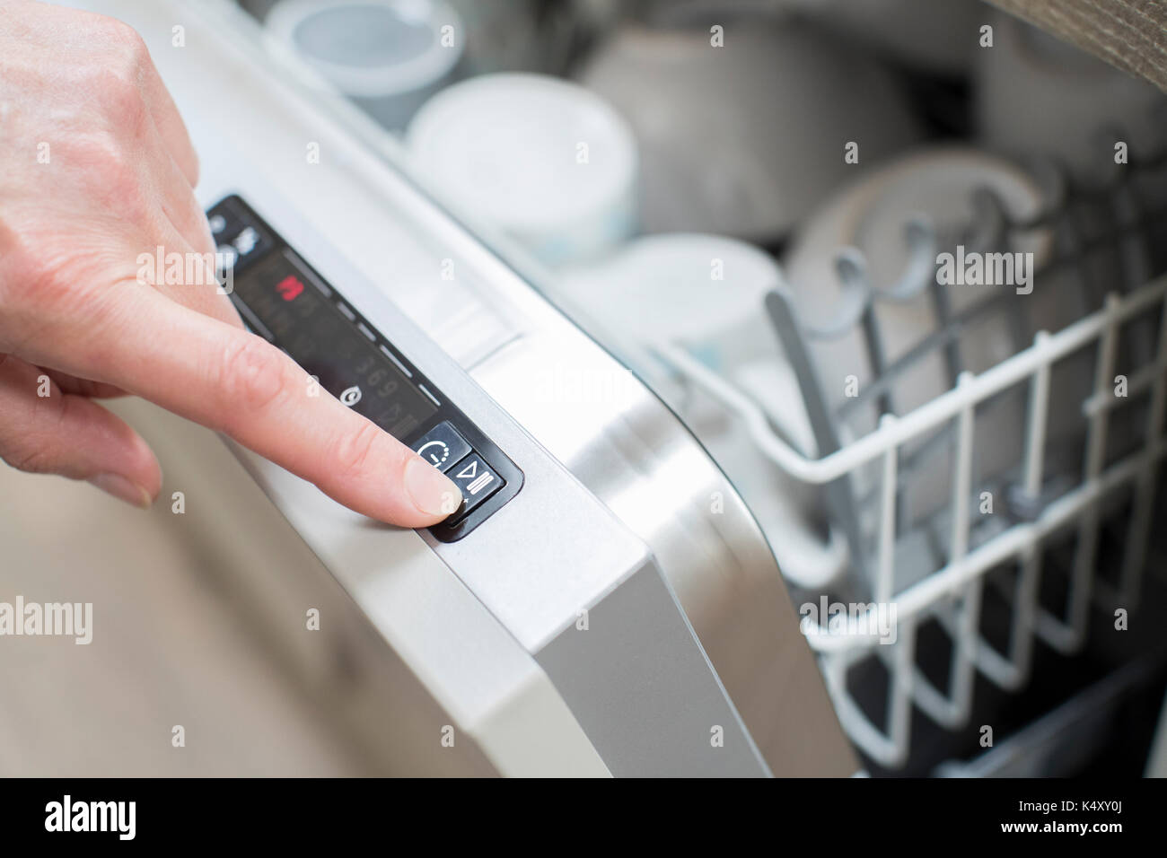 Close Up Of Woman’s Hand Pressing Start Button On Dishwasher Stock Photo
