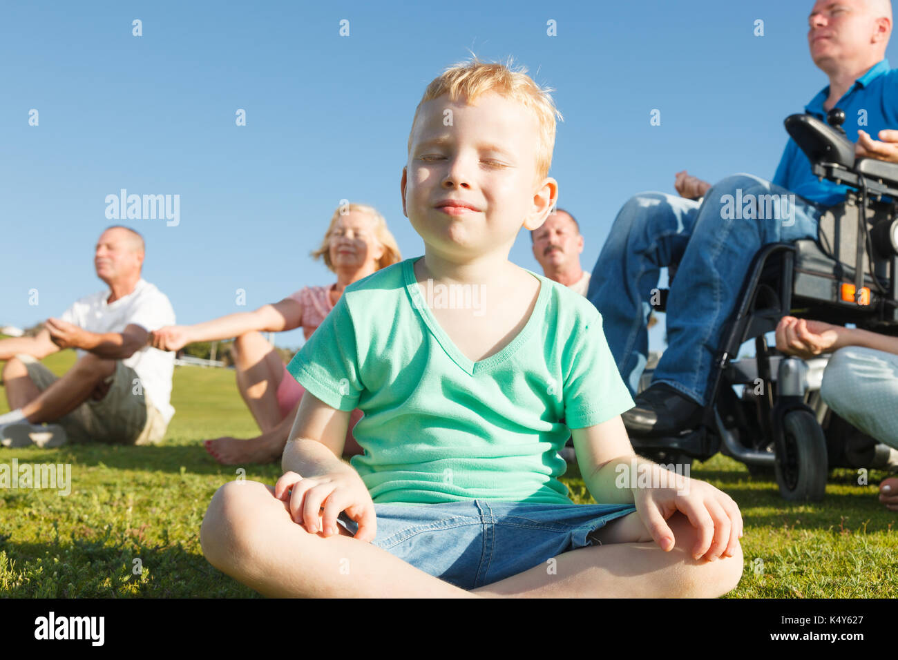 Child and group of people with disabled man practicing yoga. Stock Photo