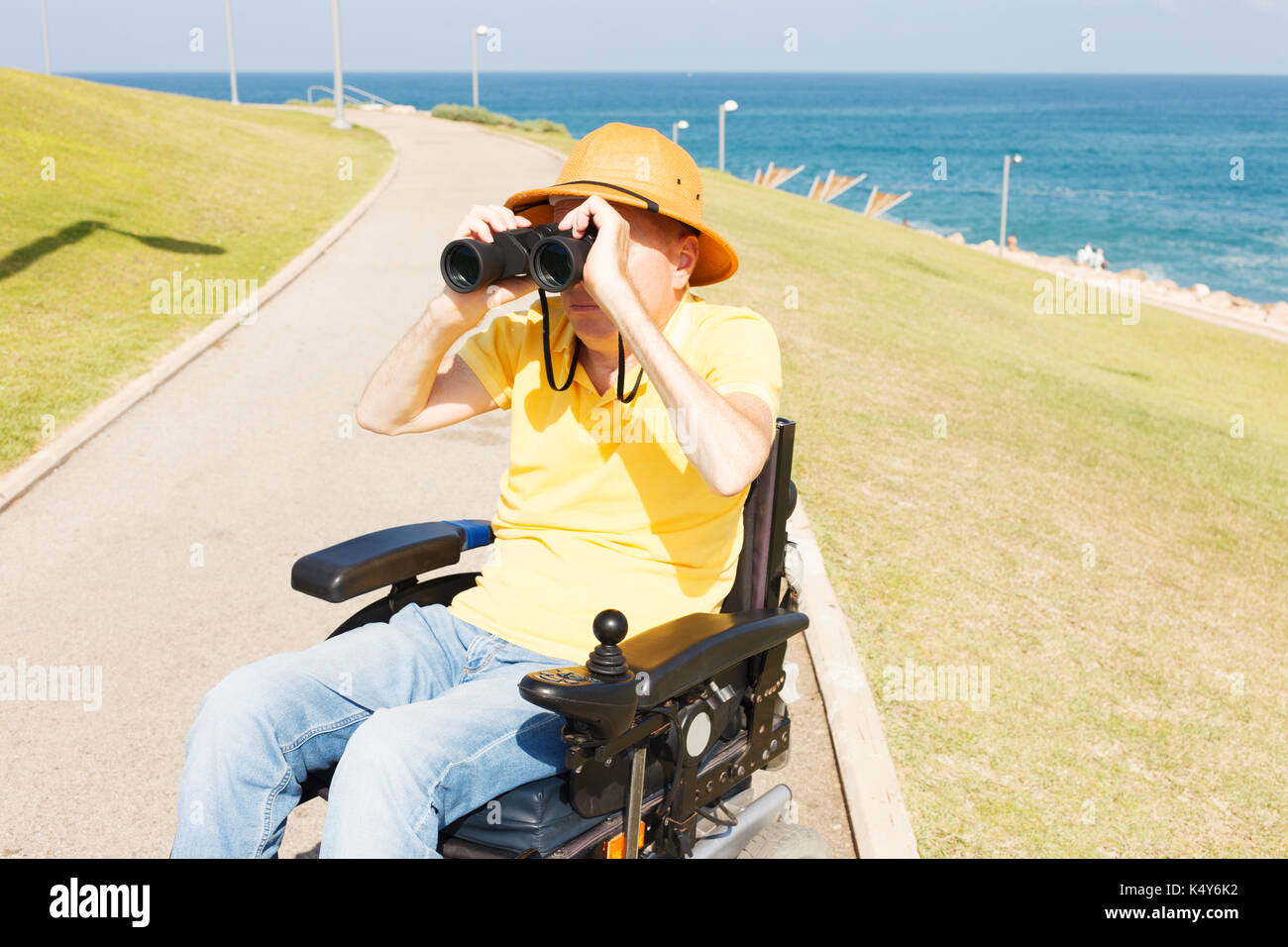 Disabled man with binocular sitting on the wheelchair. Sea on the background Stock Photo