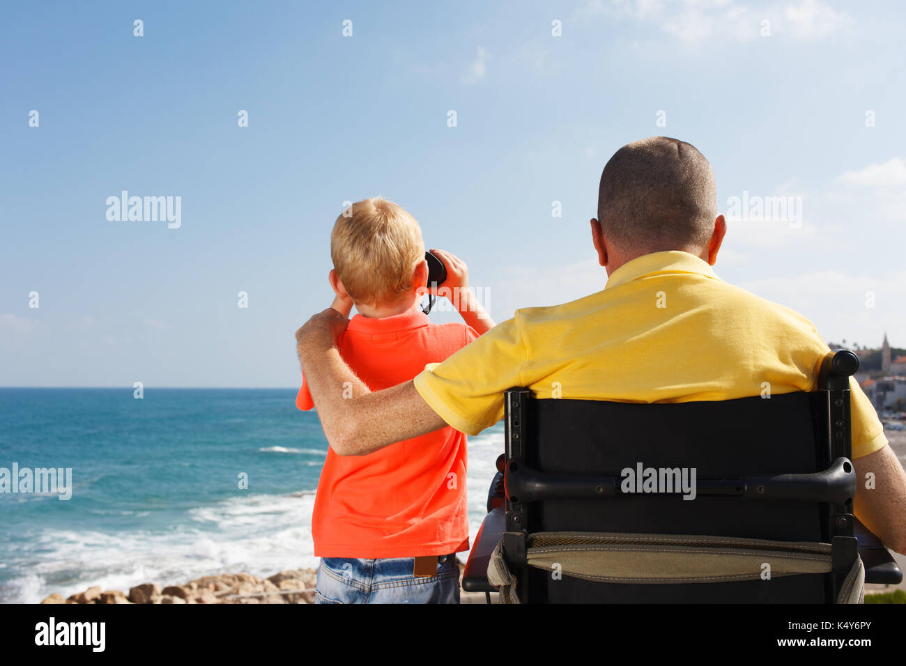 Young boy looking through binoculars with his disabled father Stock Photo