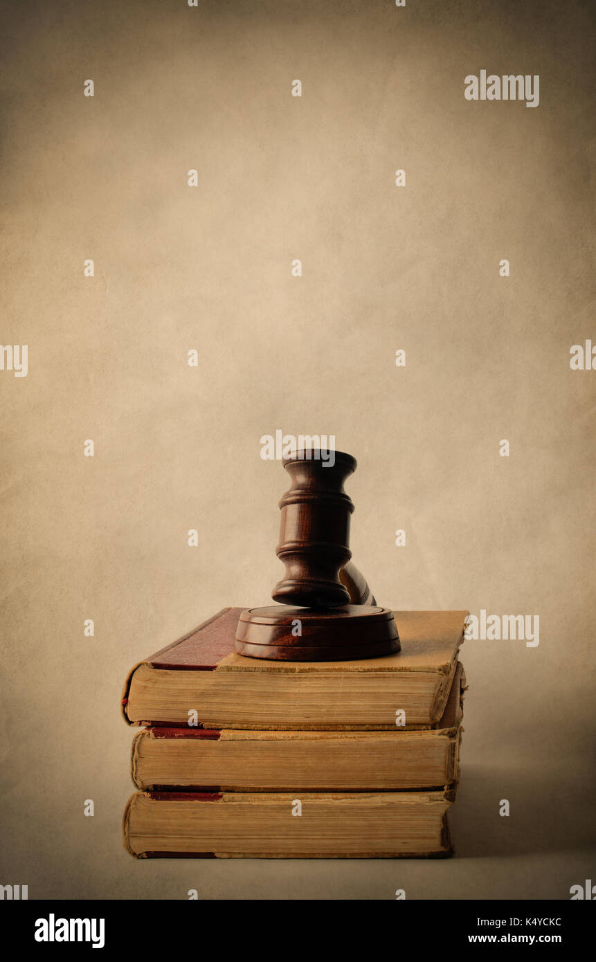 Legal concept. A wooden gavel on top of a pile of old, yellowed books. Aged parchment background and vignette for vintage effect. Stock Photo