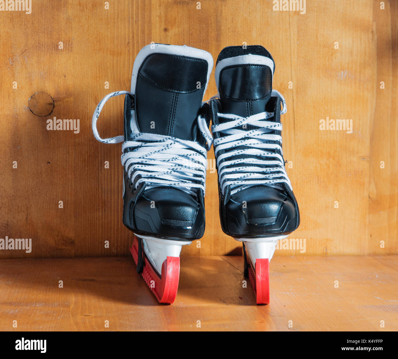 Professional hockey skates with red protective covers, against the wooden background Stock Photo