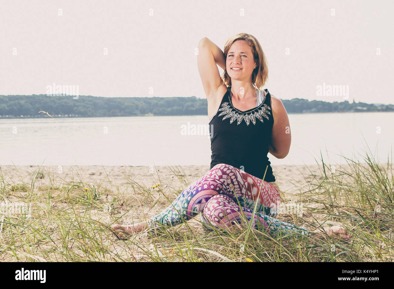 Young fit woman exercises yoga on the beach dune early morning in Germany Stock Photo