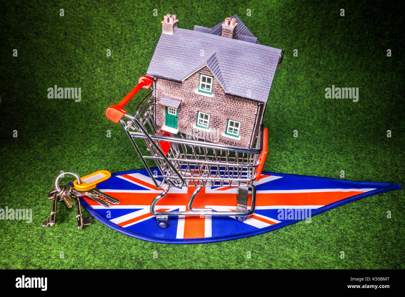 Model house in a model shopping trolley, with house keys, on Union Jack colours. A concept to depict the UK housing market of home buying or renting. Stock Photo
