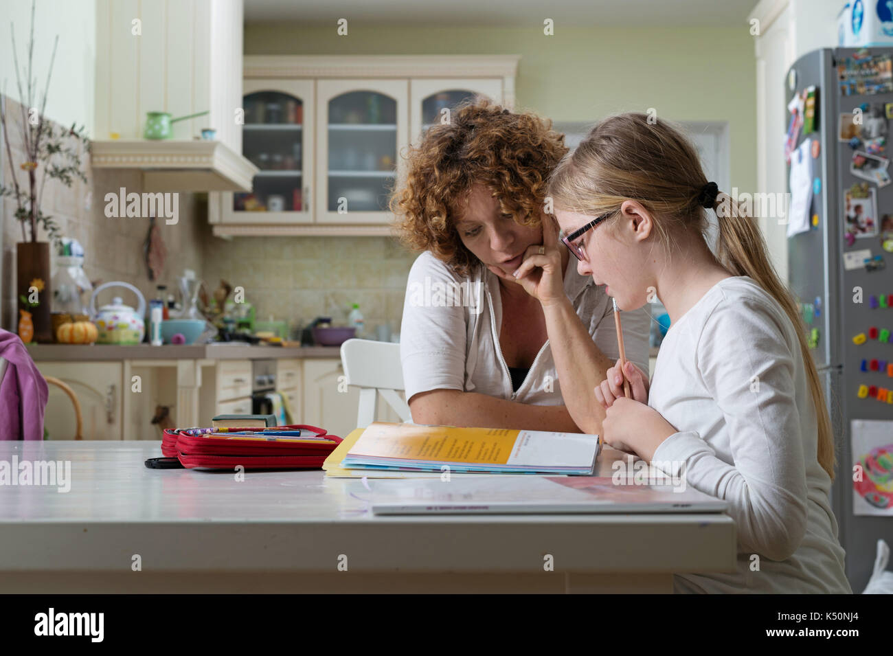Mother helping daughter with her homework at the table in the dinning ...