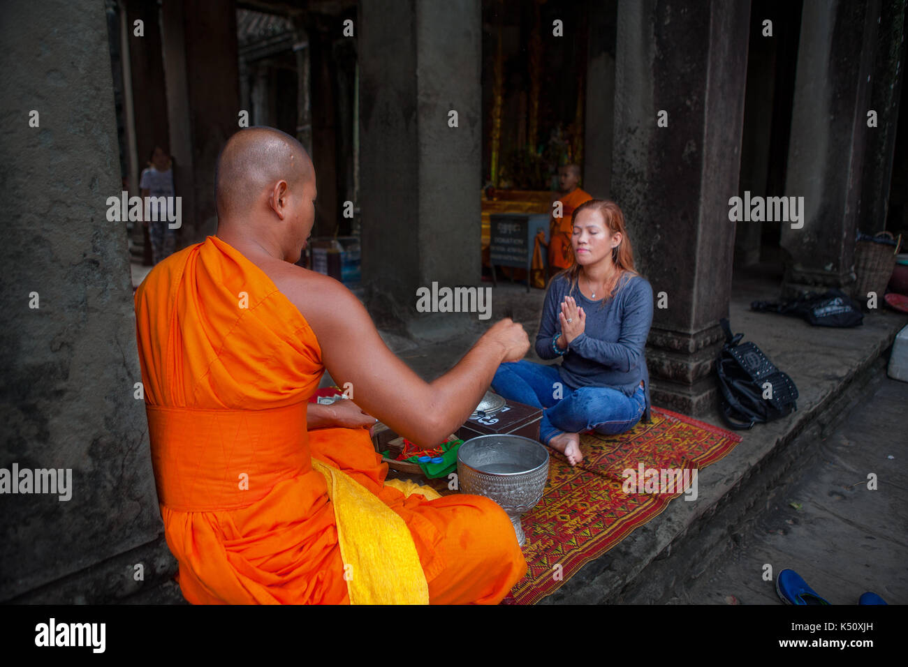 A female tourist at Angkor Wat temple complex receives a blessing from a Buddhist monk. Location is Siem Reap, Kingdom of Cambodia. Stock Photo