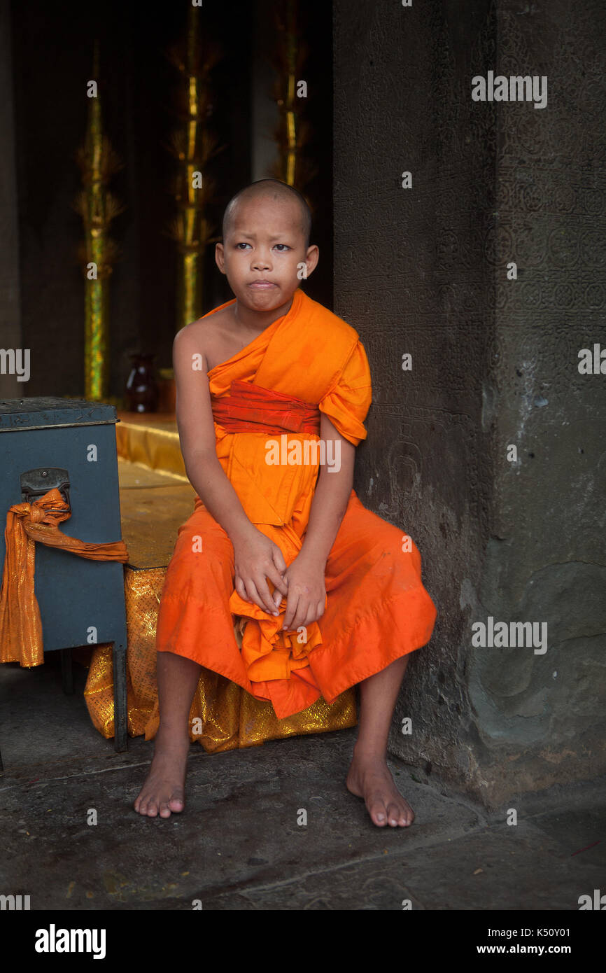 A bummed-out young Theravada Buddhist monk unhappy in his duty to protect the donation box at Angkor Wat temple in Siem Reap, Kingdom of Cambodia. Stock Photo
