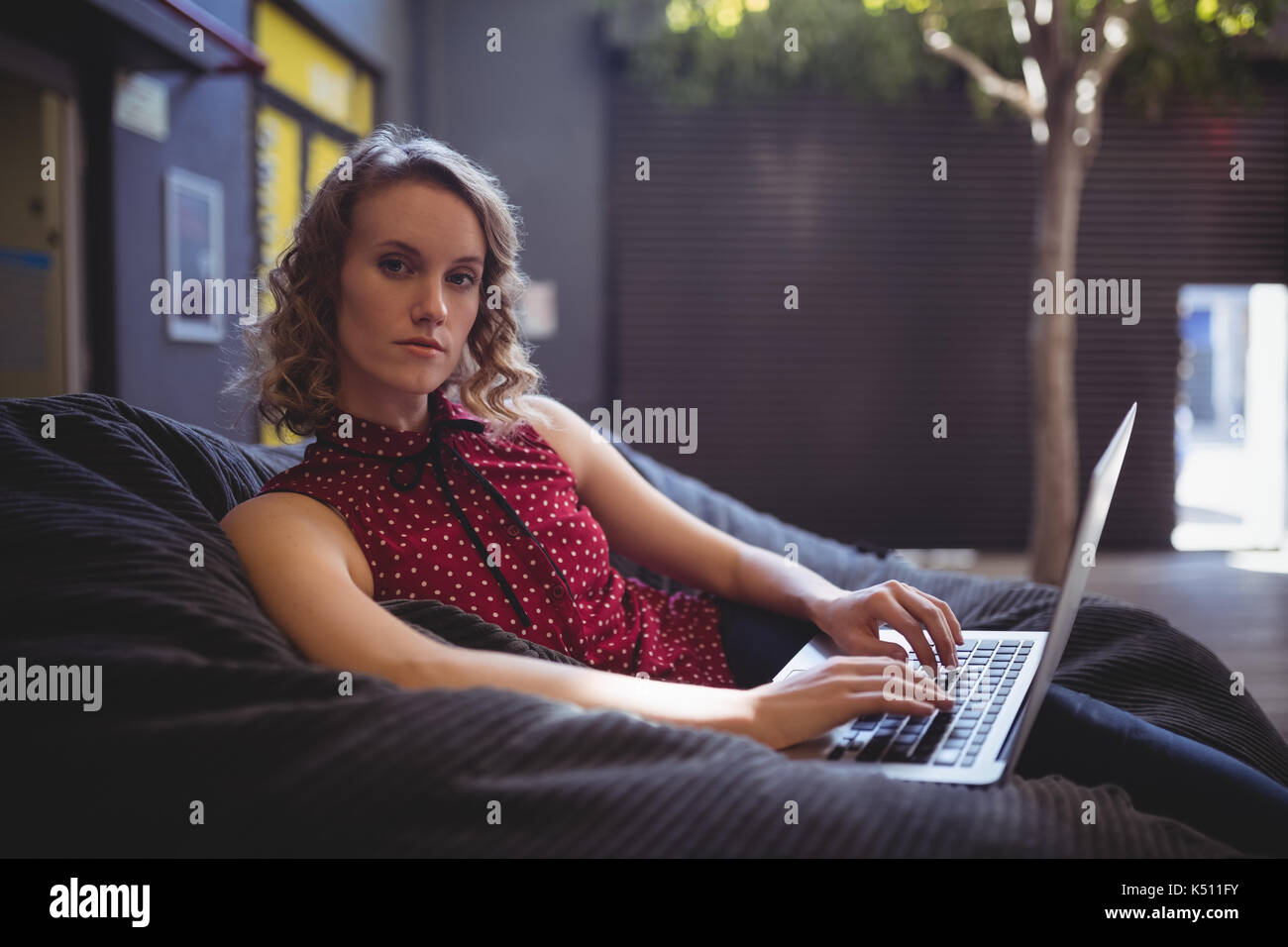 Portrait of confident young woman sitting with laptop on bean bag ...