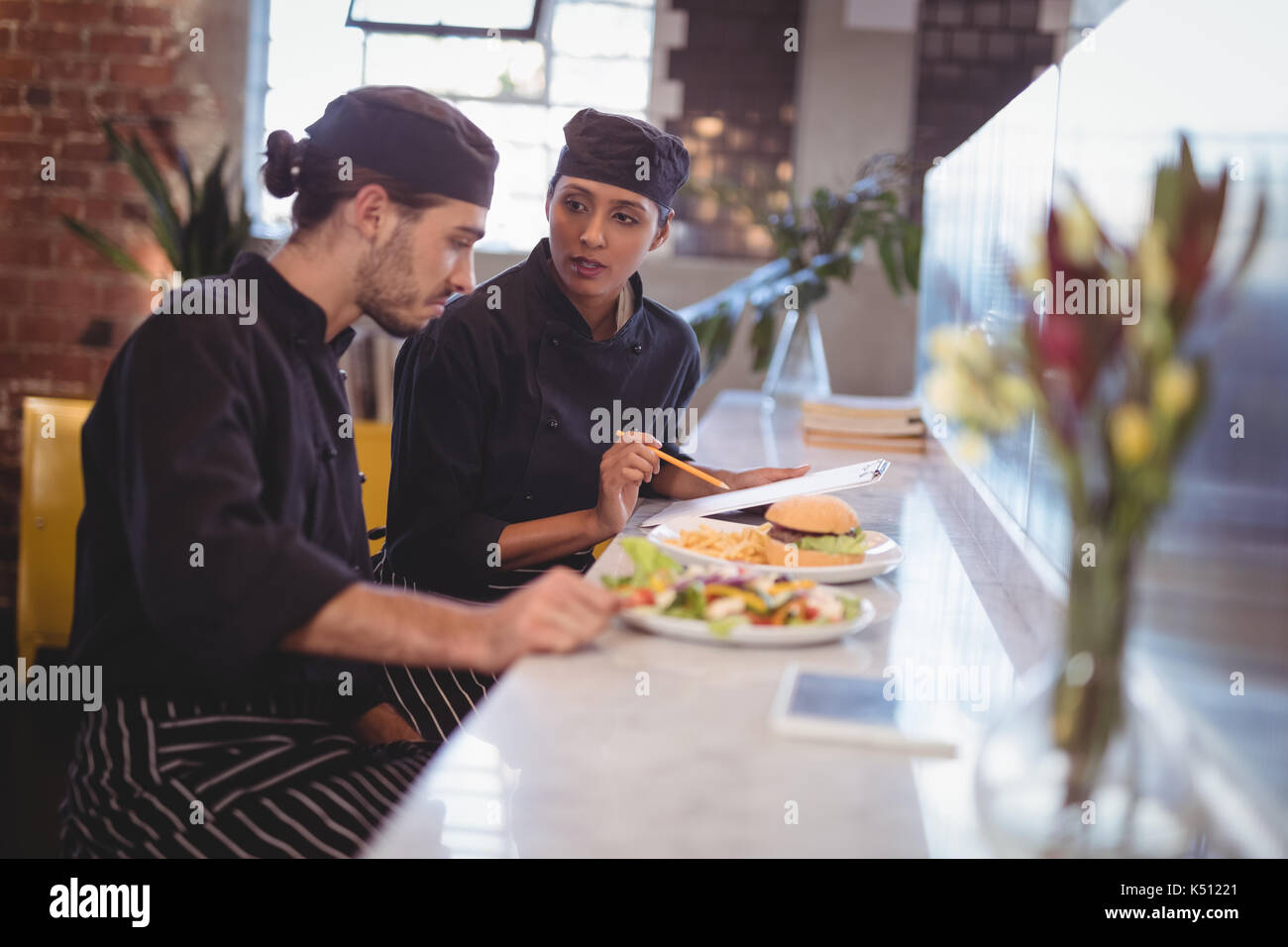 Young wait staff discussing over clipboard and food while sitting at ...