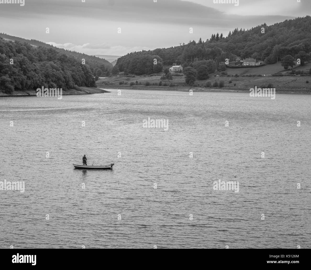 Lone fly fisherman on Ladybower Reservoir. Fly fisherman in a small lake boat, fisherman standing in the boat casting out line. Stock Photo