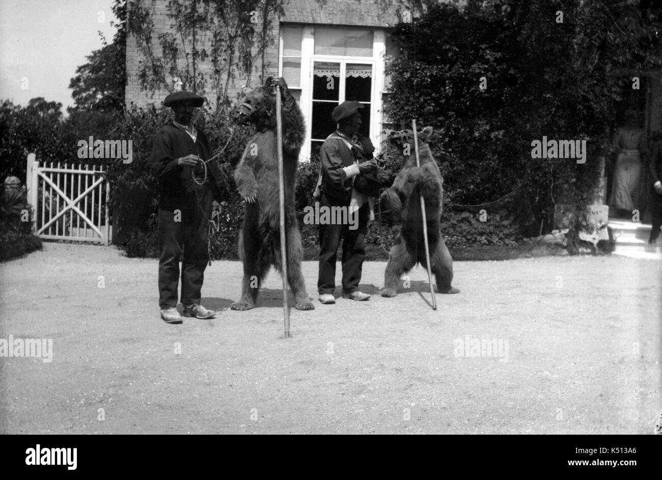 AJAXNETPHOTO. 1900 - 1910 (APPROX) LOCATION UNKNOWN. - PERFORMING BEARS - TRAINERS WEARING BASQUE TYPE BERETS AND TWO BEARS IN FRONT OF A RESIDENTIAL PROPERTY, POSSIBLY IN FRANCE. PHOTOGRAPHER:UNKNOWN © DIGITAL IMAGE COPYRIGHT AJAX VINTAGE PICTURE LIBRARY SOURCE: AJAX VINTAGE PICTURE LIBRARY COLLECTION REF:()AVL PEO PERFORMING BEARS 1900 03 Stock Photo