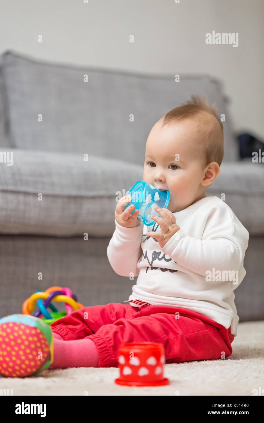 Eight months old baby girl sitting on the floor playing with her toys