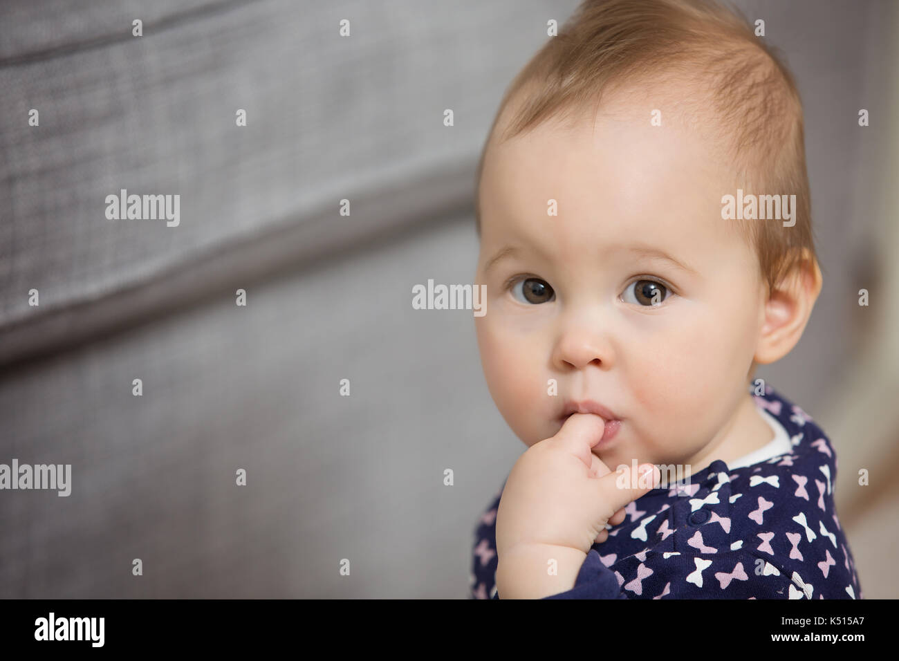 Nine months old baby girl sticking her finger in the mouth to ease the pain of teething, with eyes wide open Stock Photo