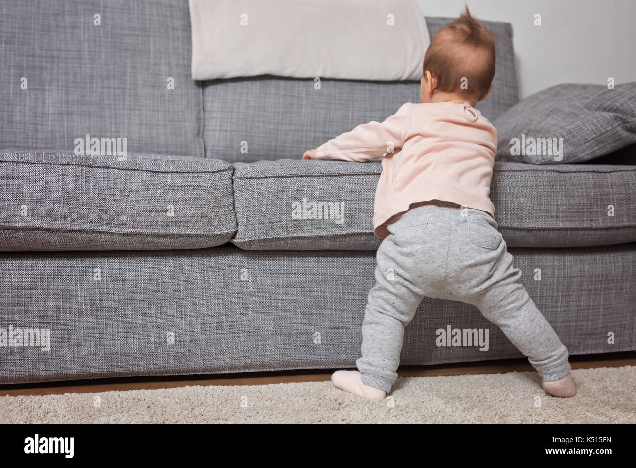 Nine months old baby girl standing on her feet in an effort to climb up