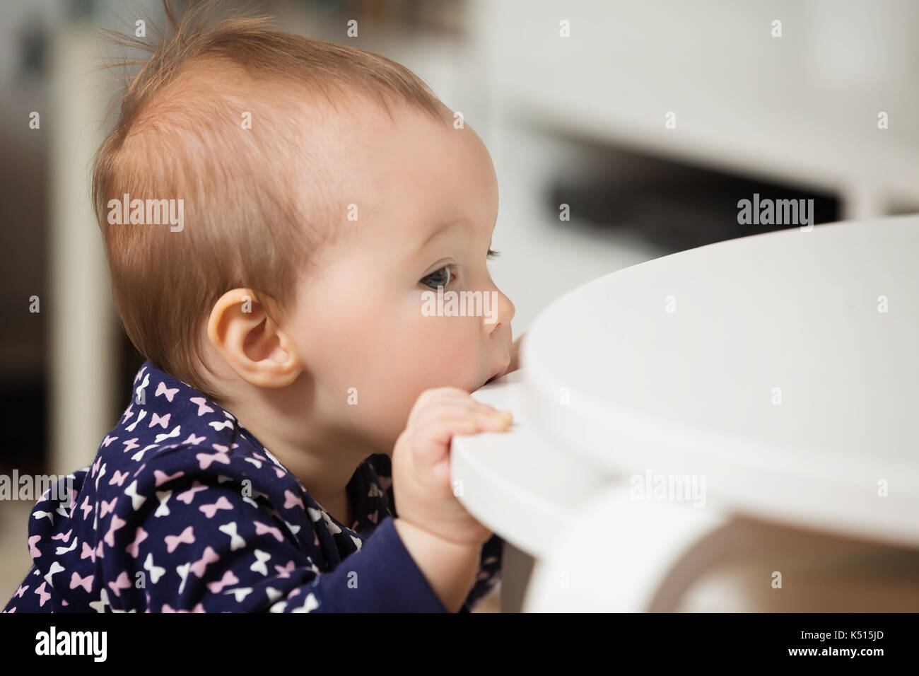 Nine months old baby girl chewing the wooden table to ease the pain of