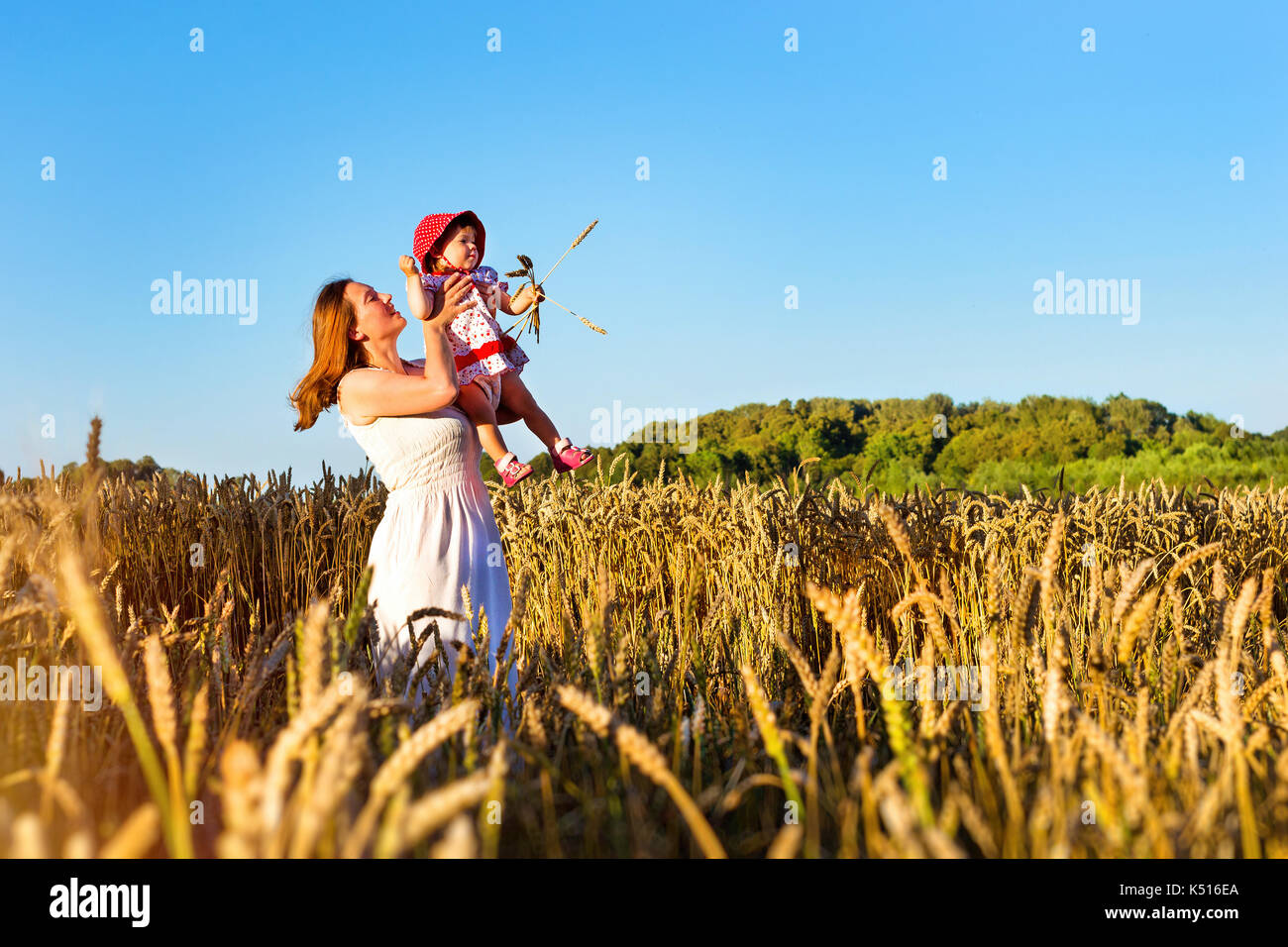 Woman with child baby in field of golden ears grain crops. Rural life, villagers to harvest. Gathered crops on field of agricultural farm. Wheat field Stock Photo