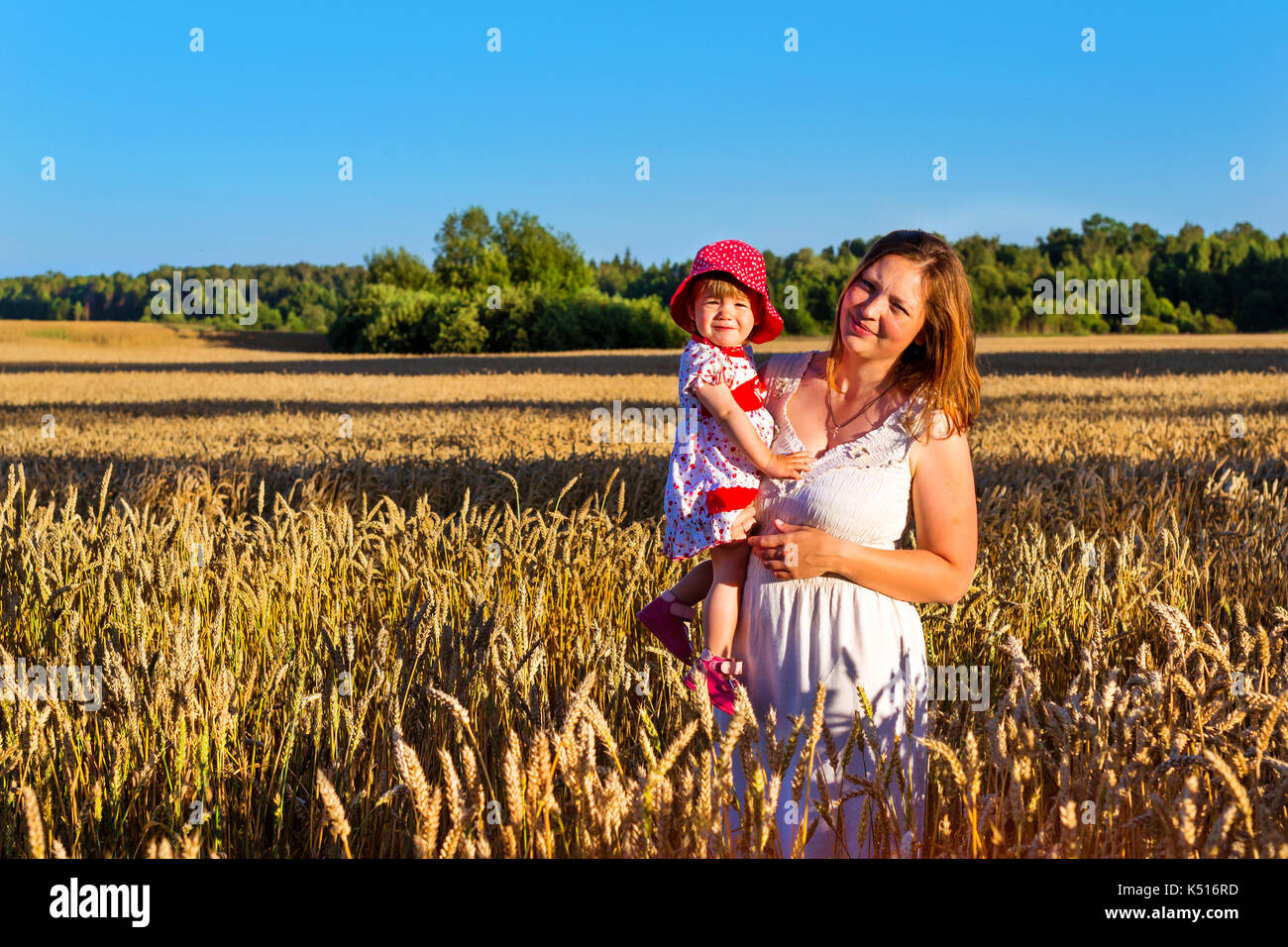 Woman with child baby in field of golden ears grain crops. Rural life, villagers to harvest. Gathered crops on field of agricultural farm. Wheat field Stock Photo