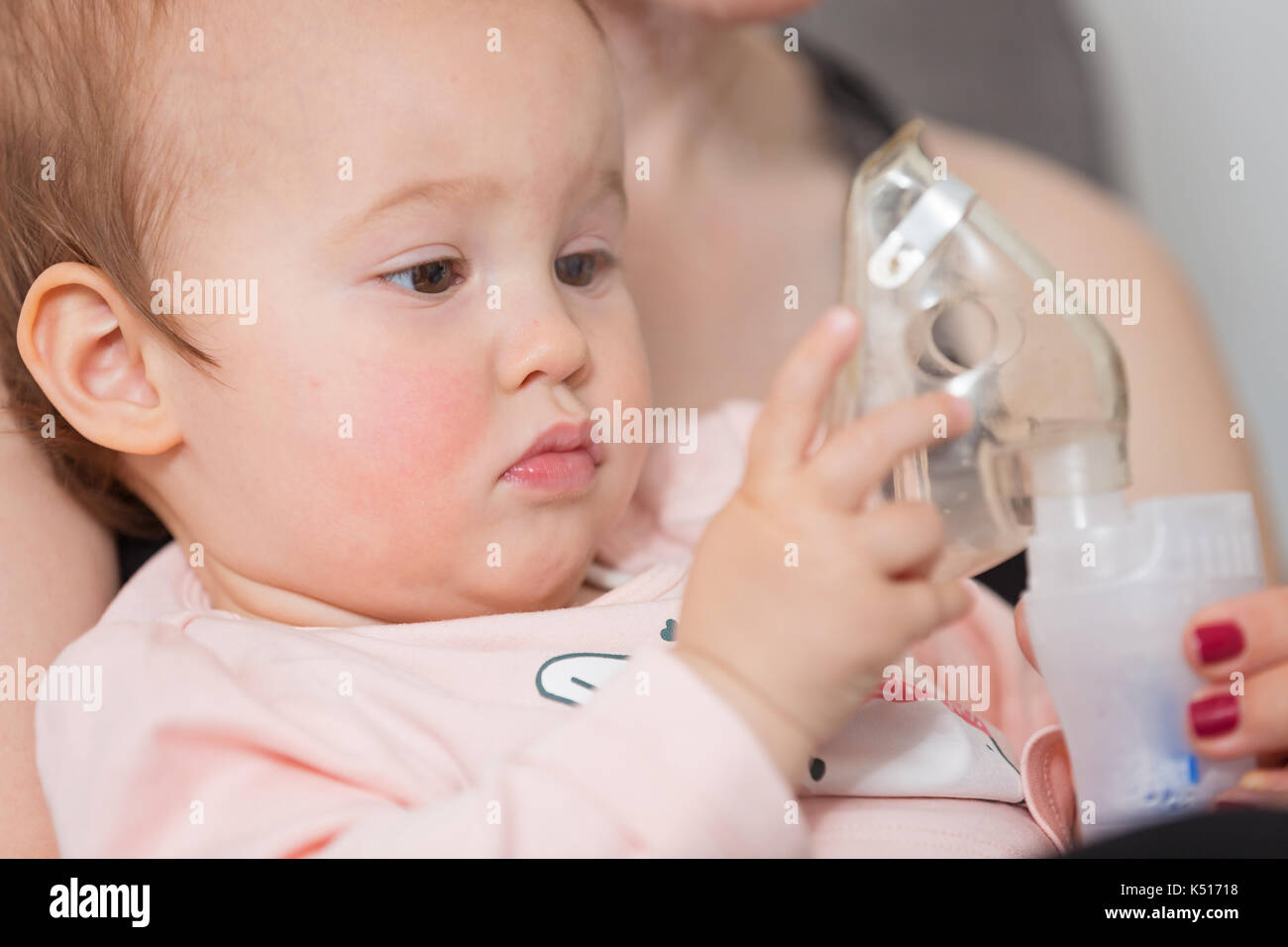Baby Using Inhaler One year old baby girl holding the inhaler, her mother holding her in ...