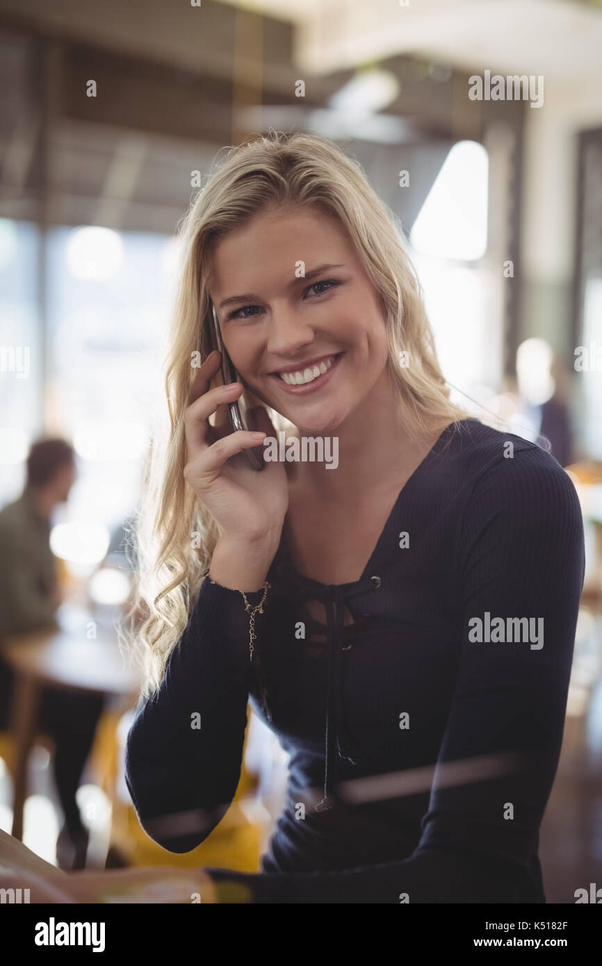 Portrait of smiling young blond woman talking on mobile phone while sitting at cafe Stock Photo