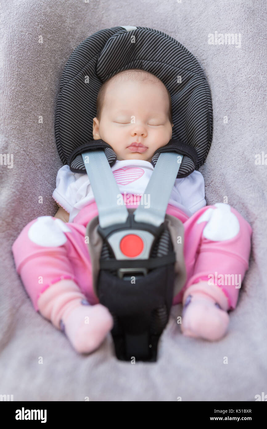 Newborn baby girl sitting in a car seat with safety belt buckled up
