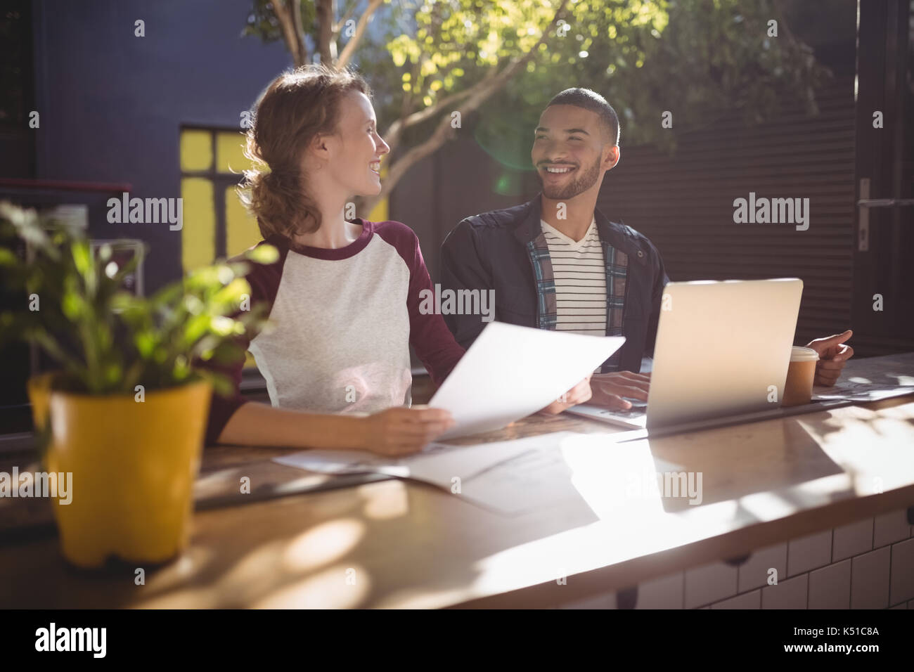 Smiling young creative professionals talking while sitting with laptop at table in coffee shop Stock Photo