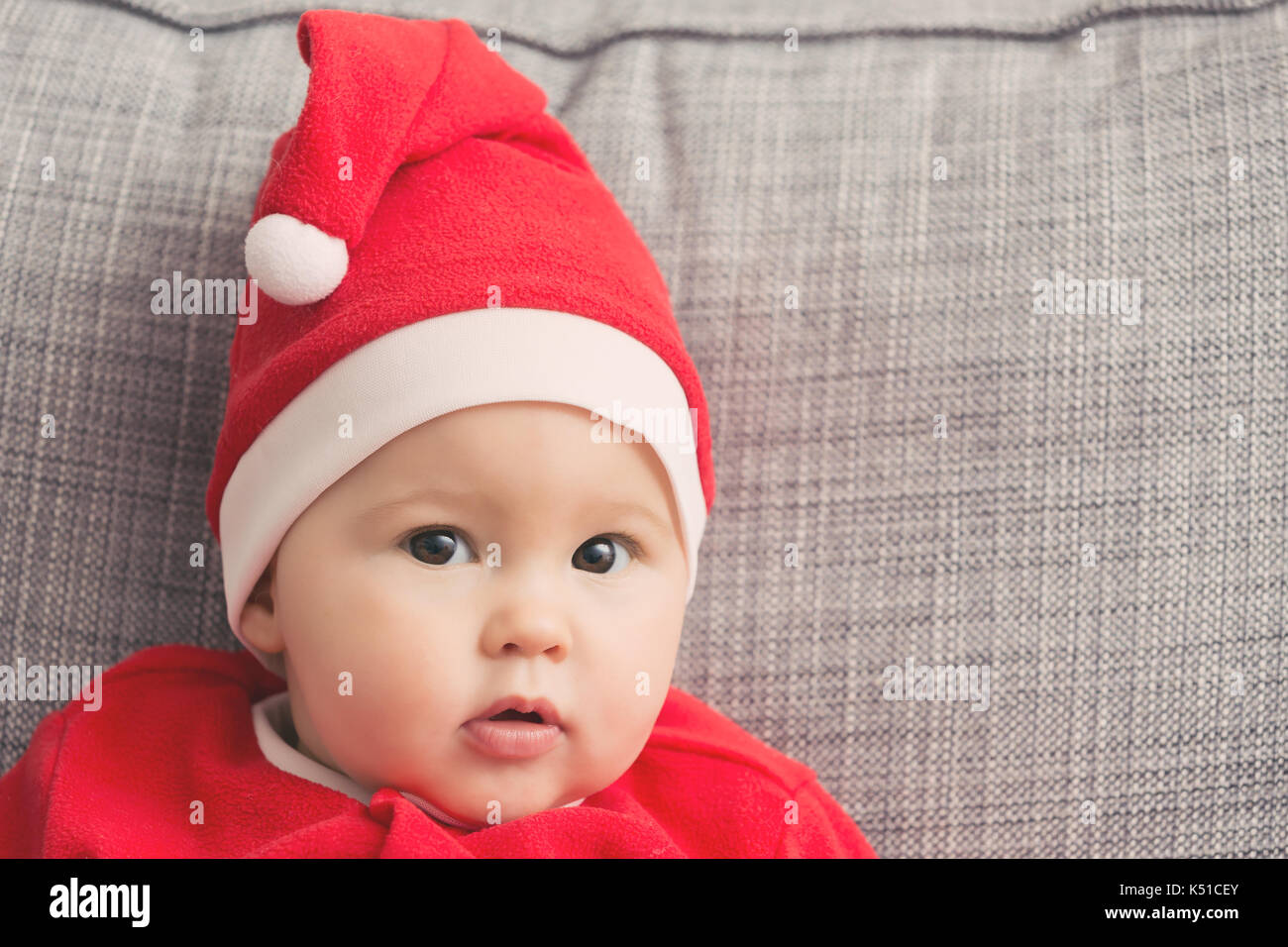Seven months old baby girl in Santa Claus dress sitting on a grey sofa